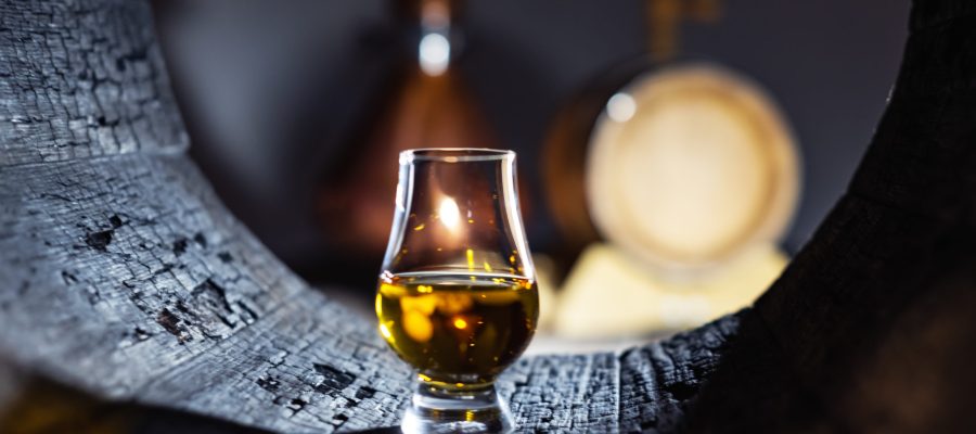 A glass of whiskey in old oak barrel. Copper alambic on background. Traditional alcohol distillery concept