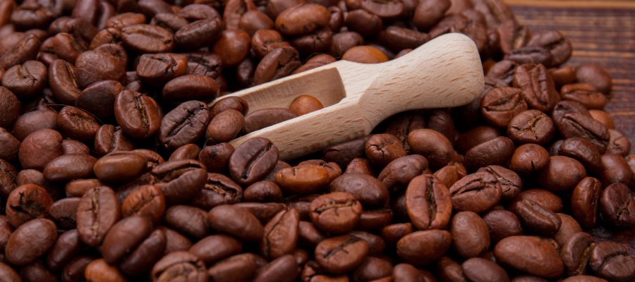 Close up small wooden spoon or scoop with coffee beans. Short wooden scoop and brown grains.