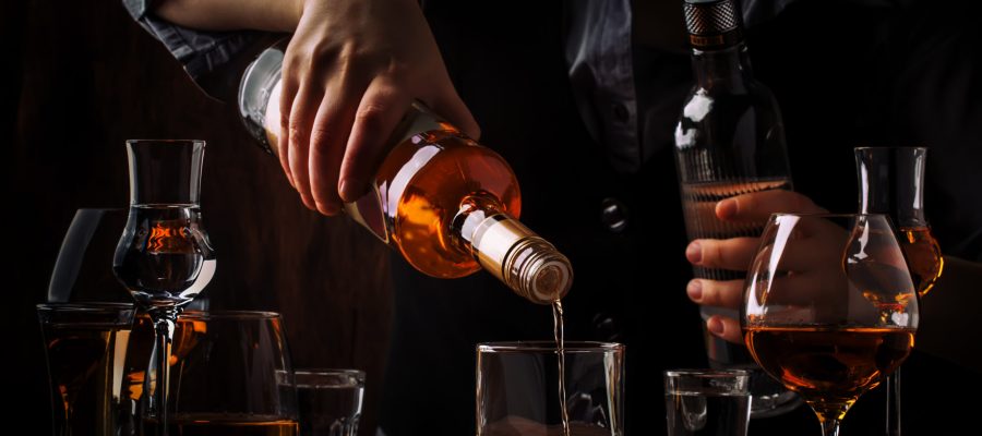The bartender pours the dark golden rum in glass on the old bar counter. Vintage wooden background in pub or bar, night mood. Place for text, toning, selective focus